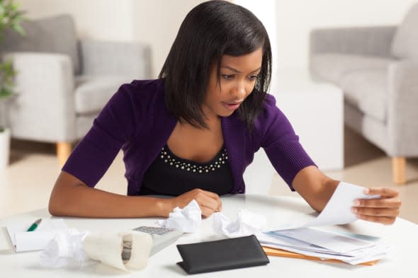 young African American woman working on finances at home wearing purple jacket sitting at dining table.