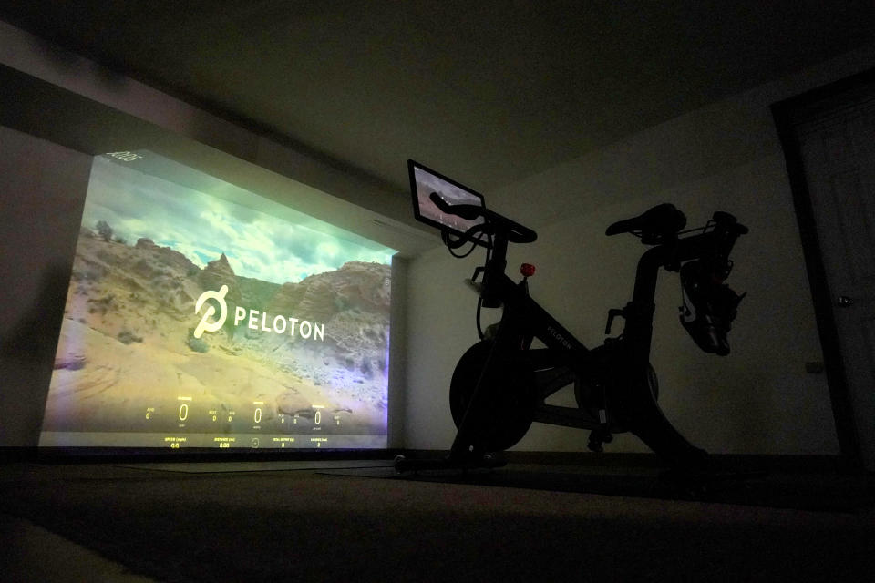 A projection of a desert scene is casted onto a wall near a Peloton fitness bike in a basement home gym, Tuesday, Sept. 15, 2020, in Lutherville-Timonium. Home gyms have picked up in 2020 with sales of exercise bikes going up during the COVID-19 pandemic. (AP Photo/Julio Cortez)