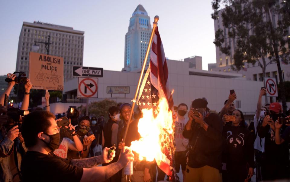 A man burns an upsidedown US flag as protesters gather in downtown Los Angeles - AFP