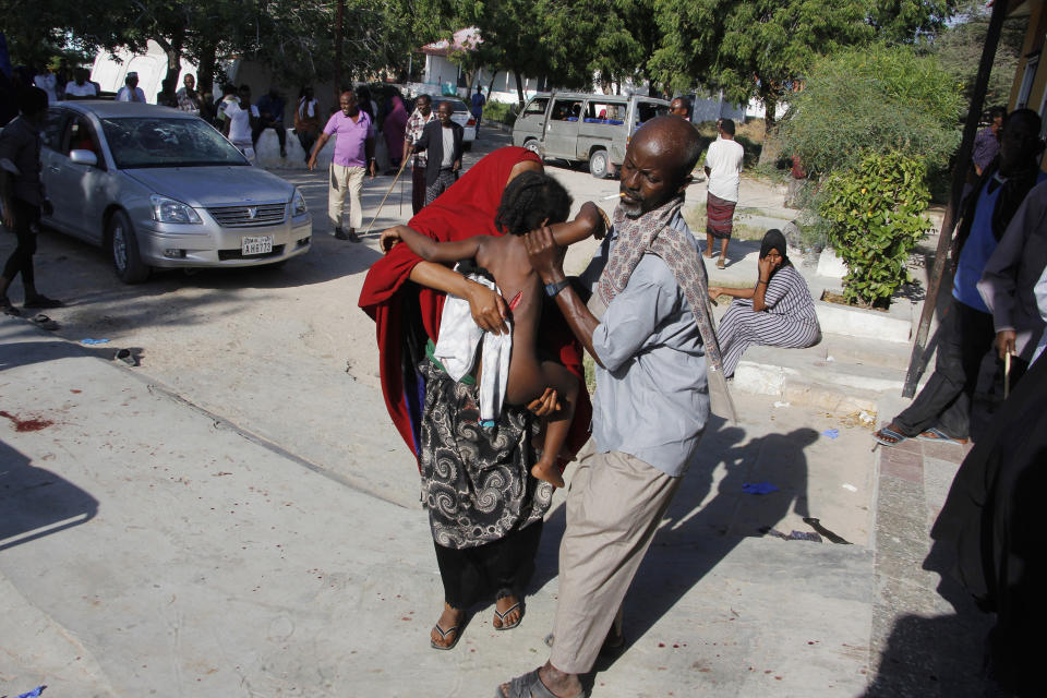 A civilian with child who was wounded in suicide car bomb attack is helped at check point in Mogadishu, Somalia, Saturday, Dec, 28, 2019.A police officer says a car bomb has detonated at a security checkpoint during the morning rush hour in Somalia's capital. (AP Photo/Farah Abdi Warsame)