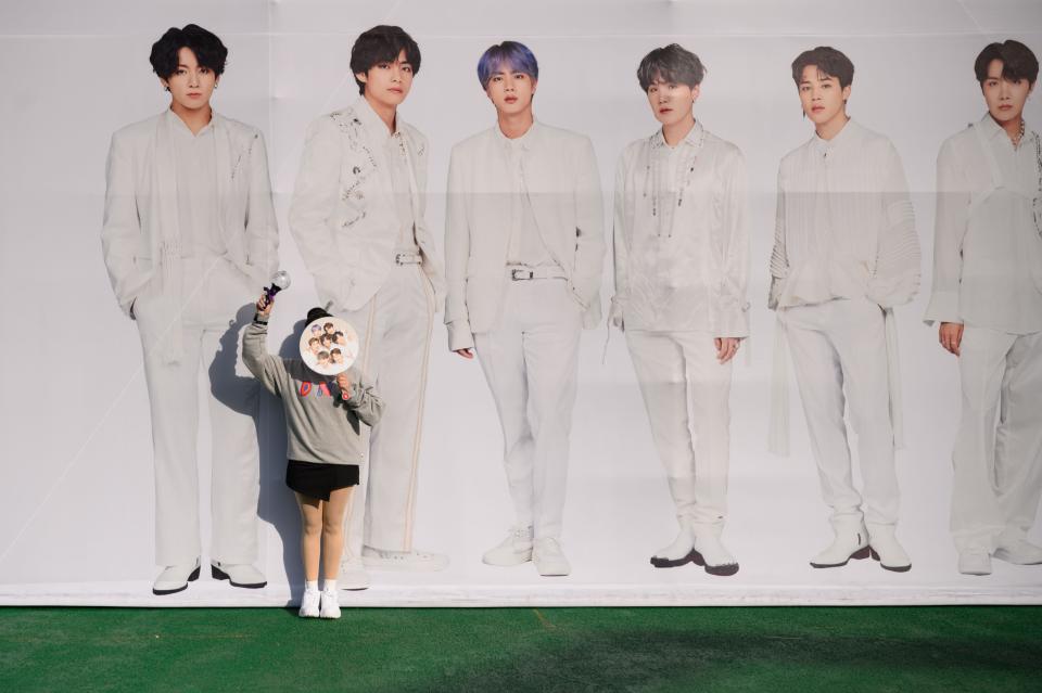 A fan of South Korea's BTS K-pop group poses for photos against a backdrop featuring an image of the band members, as they arrive for the final concert of their world tour at the Olympic stadium in Seoul in 2019.