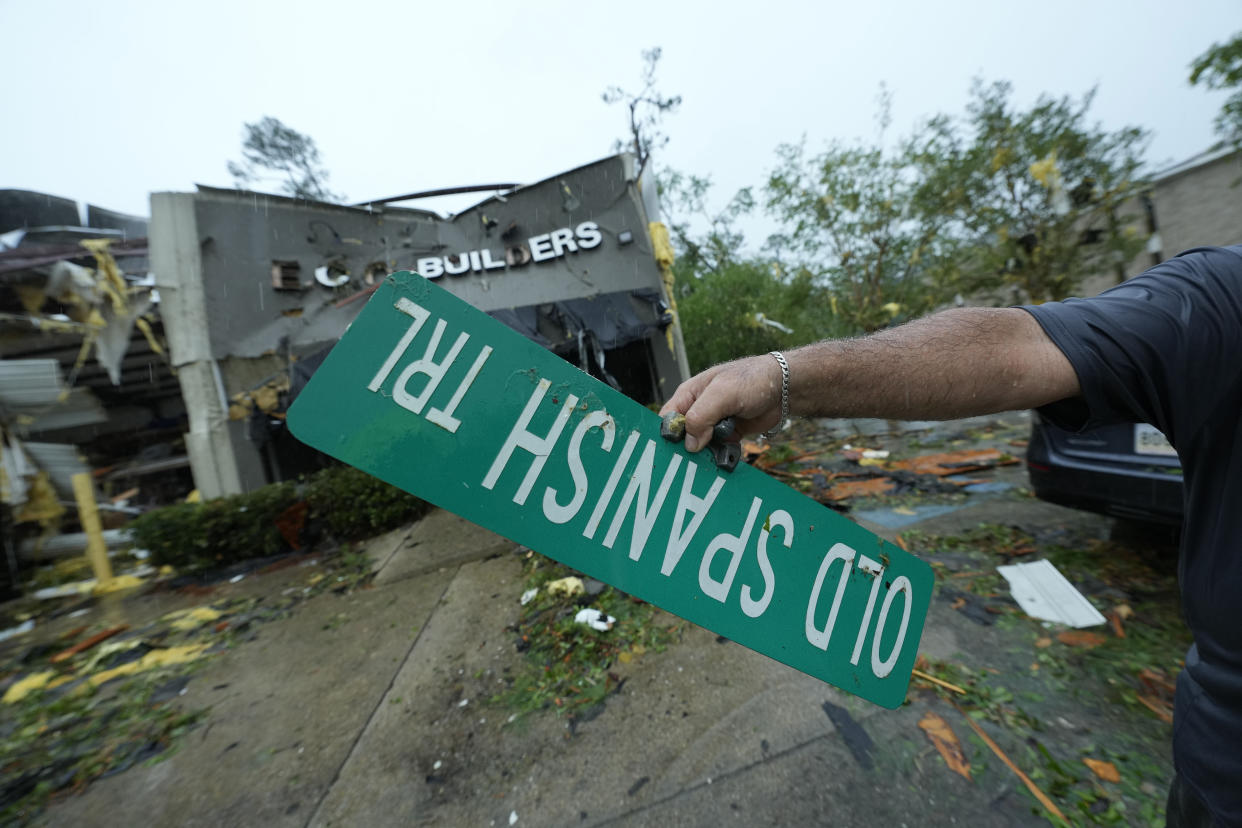 A man holds a street sign outside a damaged building in the aftermath of a tornado in Slidell, La., on Wednesday. 