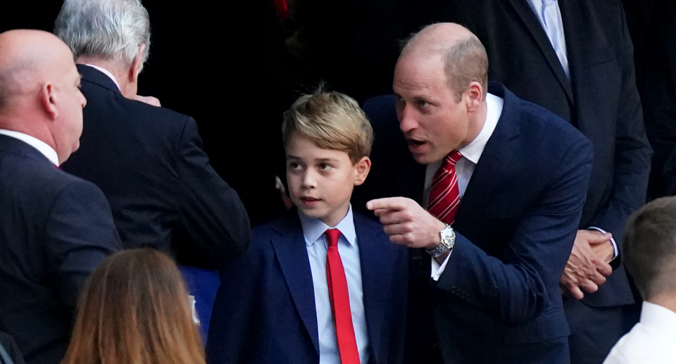 Prince William points his figure as he stands beside Prince George explaining something to him in a crowd