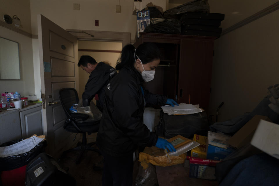 Arusyak Martirosyan, center, and Dennis Cotek, investigators with the Los Angeles County Public Administrator's office, search through a cramped micro-apartment in Los Angeles, Wednesday, Dec. 13, 2023, after a tenant was found dead in his bed with no apparent next of kin. (AP Photo/Jae C. Hong)