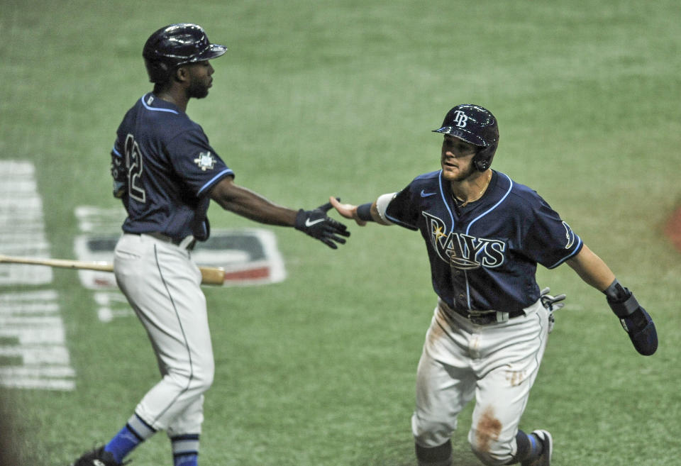 Tampa Bay Rays' Randy Arozarena, left, reaches to congratulate Mike Brosseau, right, who scores on Austin Meadow's RBI-single off Texas Rangers' Jordan Lyles during the third inning of a baseball game Thursday, April 15, 2021, in St. Petersburg, Fla. (AP Photo/Steve Nesius)
