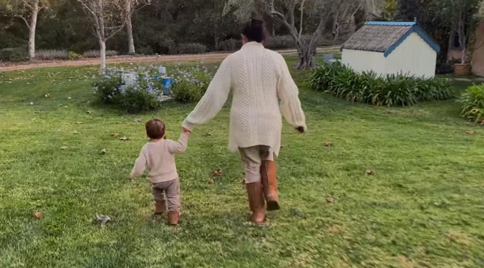 <p>Meghan and Archie hold hands as they run through a lawn, wearing coordinating neutral outfits. </p>