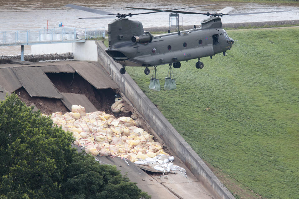 An RAF Chinook helicopter drops aggregate to help shore up a reservoir at risk of collapse, threatening to engulf the town of Whaley Bridge in the Peak District, England, Friday, Aug. 2, 2019. A British military helicopter has dropped sandbags to shore up a reservoir wall as emergency services worked frantically to prevent a rain-damaged dam from collapsing. Engineers say they remain "very concerned" about the integrity of the 19th-century Toddbrook Reservoir, which contains around 1.3 million metric tons (1.5 million (U.S tons) of water. (AP Photo/Jon Super)