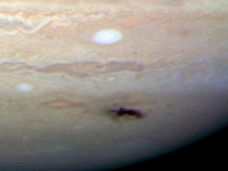 jupiter surface close-up shows long dark purple spot in the pale orange surface