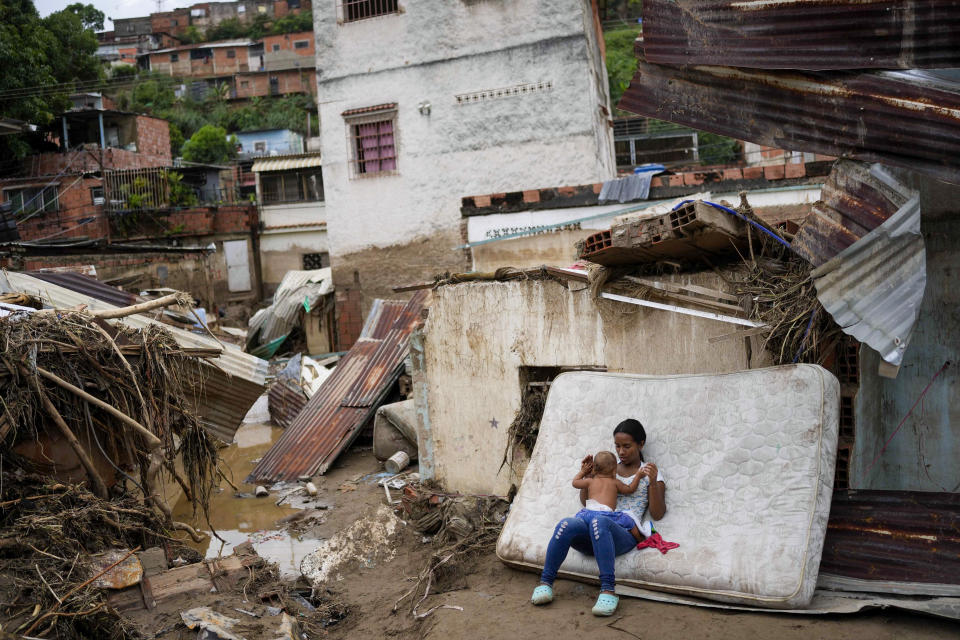 A woman holds a baby in front of her home damaged by flooding in Las Tejerias, Venezuela, Sunday, Oct. 9, 2022. At least 22 people died after intense rain caused flash floods and the overflow of a ravine, Vice President Delcy Rodríguez said. (AP Photo/Matias Delacroix)