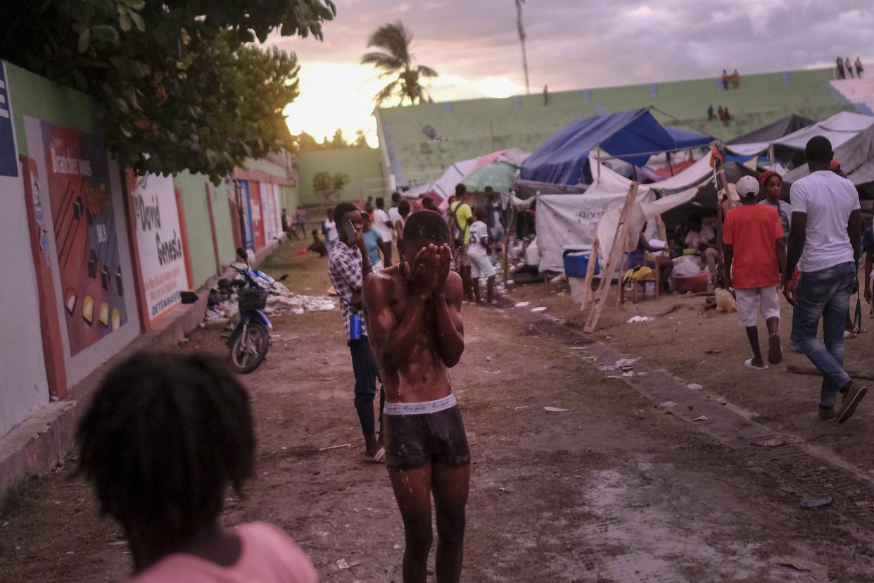 A youth bathes at a makeshift camp for people whose homes collapsed during the earthquake at a soccer field at sunset in Les Cayes, Haiti, Monday, Aug. 16, 2021, two days after a 7.2-magnitude earthquake struck the southwestern part of the country.