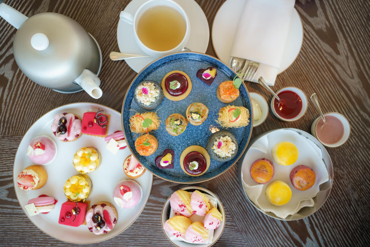 Top view of afternoon tea, cakes and snacks with a teapot in the background.