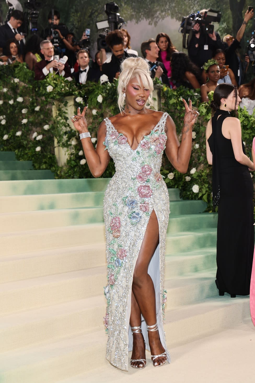 Aya Nakamura wears an ivory dress encrusted in pearlescent flowers. Her wig and eyebrows are dyed a vivid shade of blonde.