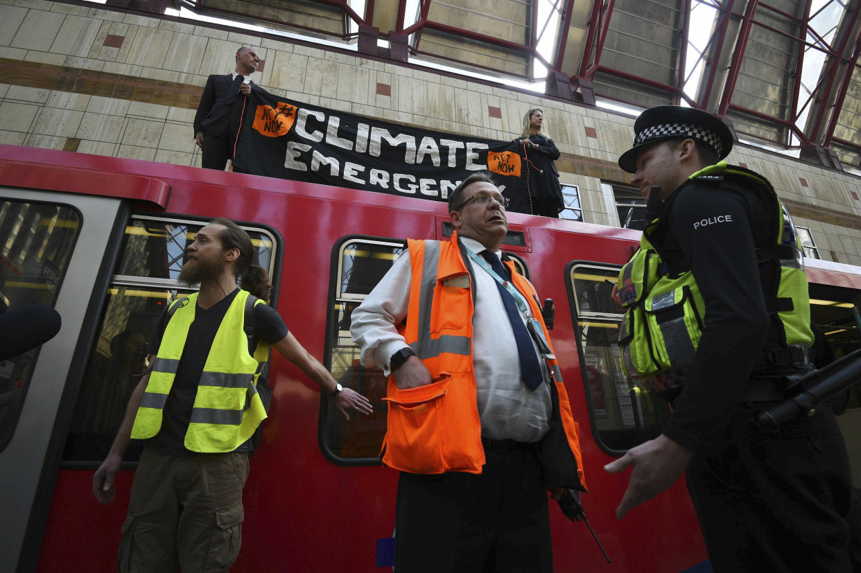 Police and officials stand by as climate activists protest atop a Dockland Light Railway carriage at Canary Wharf station in London, as part of the ongoing climate change demonstrations in the capital, Wednesday April 17, 2019. The environment protest group Extinction Rebellion are calling for general public protests with civic disobedience held over several days, to highlight what it says is the failure to tackle the causes of climate change. (Kirsty O'Connor/PA via AP)