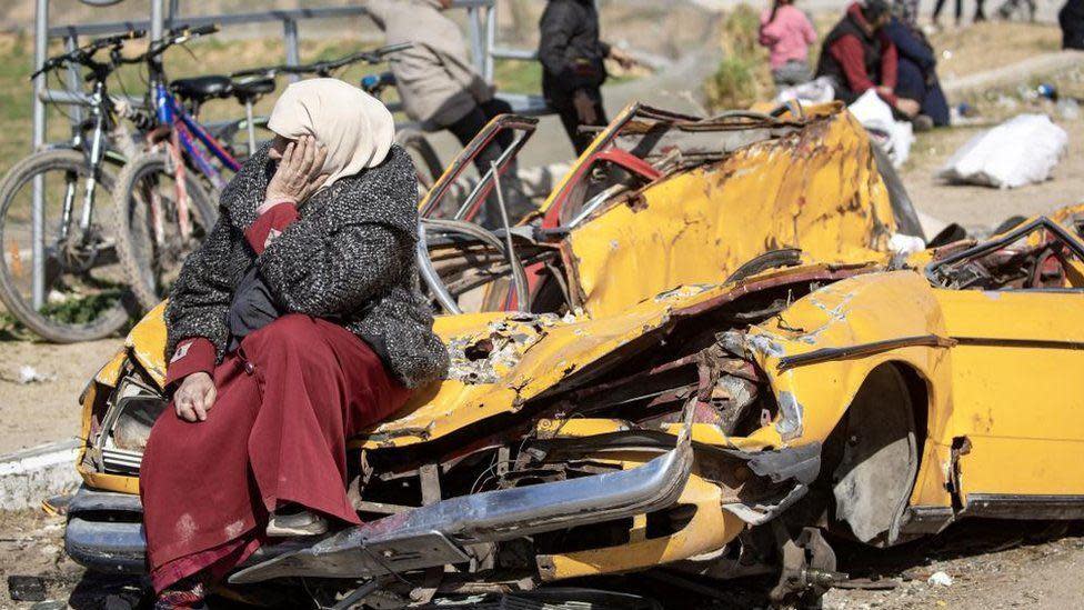 Una mujer junto a un auto destrozado en Gaza.