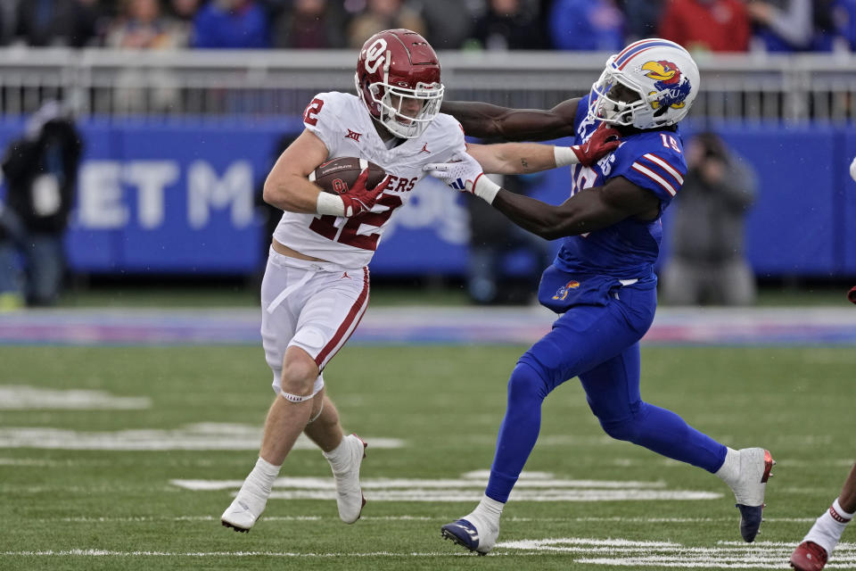 Oklahoma wide receiver Drake Stoops (12) is chased by Kansas linebacker Craig Young (15) during the first half of an NCAA college football game Saturday, Oct. 28, 2023, in Lawrence, Kan. (AP Photo/Charlie Riedel)