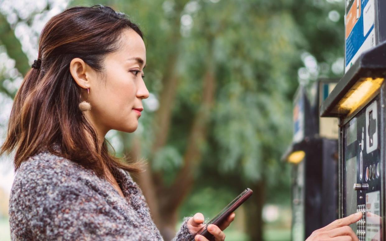 A driver making a contactless payment by smartphone at a parking machine on a street