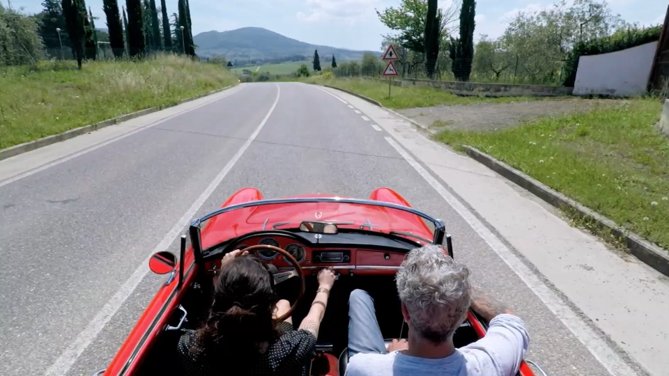 Bourdain riding in a red convertible sports car with Asia Argento