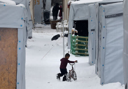 A stranded Syrian refugee child tries to move his bicycle during a snowstorm at a refugee camp north of Athens, Greece January 10, 2017.REUTERS/Yannis Behrakis