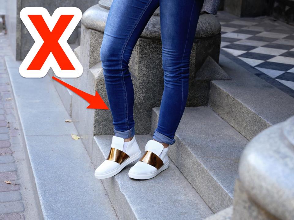 red x and arrow over person walking down steps wearing skinny jeans and white and gold sneakers