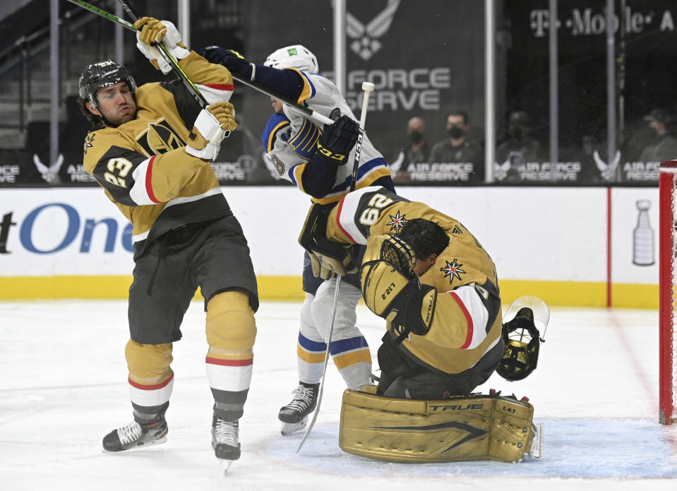 Vegas Golden Knights goaltender Marc-Andre Fleury (29) has his helmet knocked off by defenseman Alec Martinez (23) and St. Louis Blues left wing Mackenzie MacEachern (28) during the first period of an NHL hockey game Saturday, May 8, 2021, in Las Vegas. (AP Photo/David Becker)