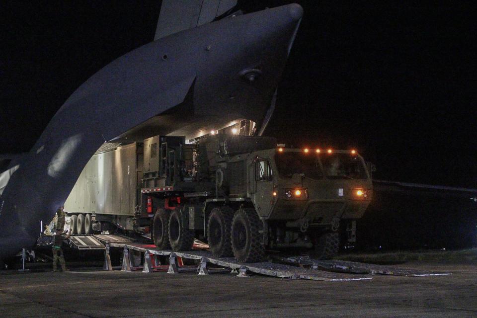 A missile launcher on wheels being unloaded from a military aircraft at night.