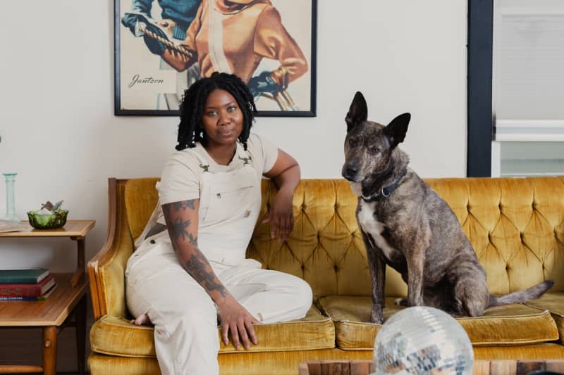 Dweller and dog sit on gold velvet couch under artwork in living room.