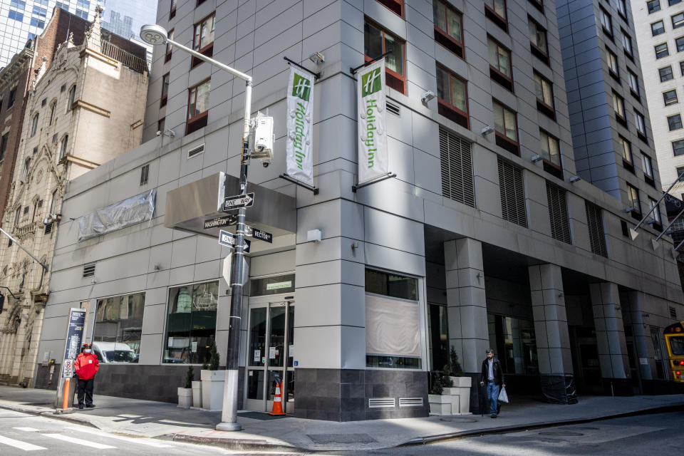 Pedestrians pass the Holiday Inn Manhattan - Financial District hotel on Rector Street, Wednesday, March 29, 2023, in New York. City officials, operating under legal mandates that require New York City to provide shelter to anyone seeking it, have turned to hotels to house busloads of international migrants seeking asylum who have been sent to the city from other states. Around Manhattan and elsewhere in the city, hotels that served tourists just a few years ago have become de facto emergency shelters. The latest is the historic Roosevelt Hotel in midtown Manhattan, which shuttered three years ago, is reopening later this week as a welcome center and shelter for asylum seekers. (AP Photo/John Minchillo)