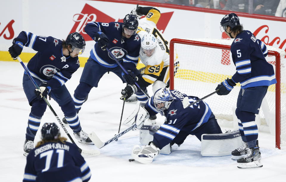 Winnipeg Jets goaltender Connor Hellebuyck (37) jumps on the puck as Pittsburgh Penguins' Jake Guentzel (59) attempts to get his stick on the rebound during first-period NHL hockey game action in Winnipeg, Manitoba, Saturday, Nov. 19, 2022. (John Woods/The Canadian Press via AP)