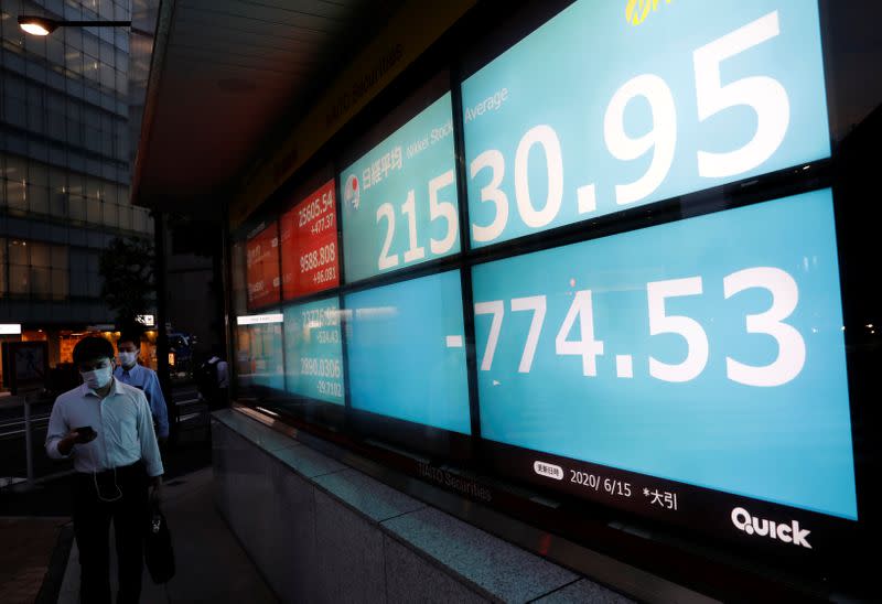 FILE PHOTO: Men wearing protective face masks, following the coronavirus disease (COVID-19) outbreak, walk past a stock quotation board outside a brokerage in Tokyo