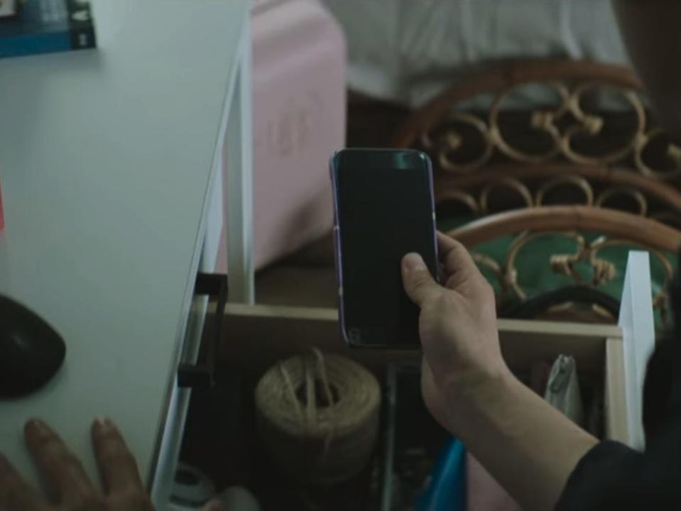 jun-yeong's hand pulling a purple cell phone out of a cluttered desk drawer and holding it up