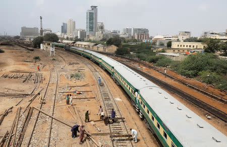 A passenger train moves past labourers working on a railway track along City Station in Karachi, Pakistan September 24, 2018. REUTERS/Akhtar Soomro