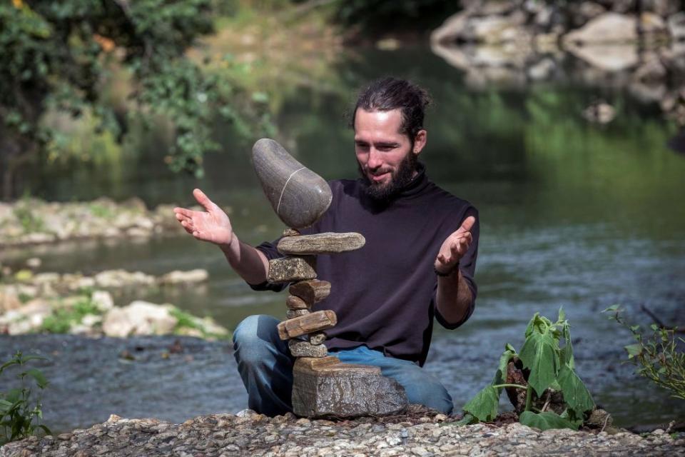 French artist and rock balancer SP Ranza looks at his temporary sculpture made of stones collected in the river on October 10, 2019 near Mazamet, southern France. - SP Ranza won the Stone Stacking European Championships in Dunbar, Scotland, last April 2019 and will take part in the llano Earth Art Festival and World Stone Balancing competition 2020. 