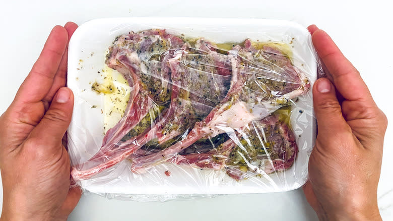 Hands holding plastic wrapped meat in marinade