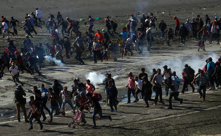 Migrants, part of a caravan of thousands from Central America trying to reach the United States, run from tear gas released by U.S border patrol, near the border fence between Mexico and the United States in Tijuana, Mexico, November 25, 2018. REUTERS/Hannah McKay