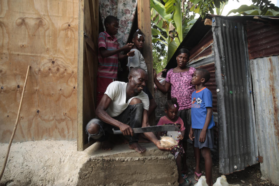 Mackenson Victor abre un coco para su hija, Manouchi Victor, el centro al frente, y sus hijastros, Myson Veillard, arriba a la izquierda, Routcheland Veillard, arriba, segunda desde la izquierda, y Dabens Veillard, al frente a la derecha, ante la mirada de su pareja, Renèse Estève, en su casa en una zona rural de Saint-Louis-du-Sud, Haití, el jueves 25 de mayo de 2023. Dos de los cuatro hijos de Estève, que no aparecen en la imagen, se reunieron con la familia en una casa de una habitación tras pasar tres años en un orfanato. (AP Foto/Odelyn Joseph)