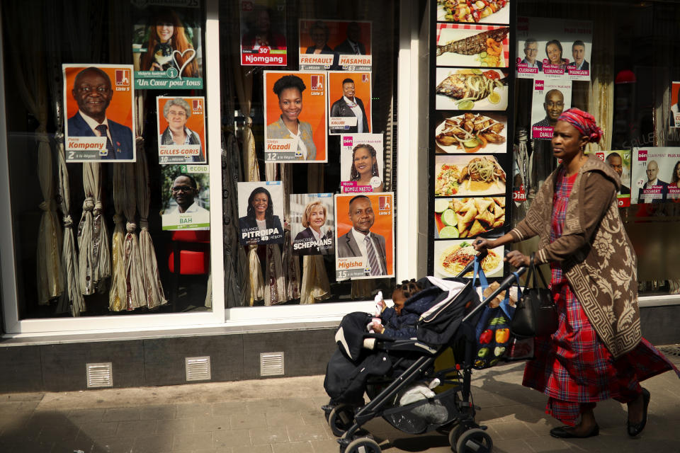 A woman walks past political campaign posters placed on a restaurant window at the African Matonge quarter in Brussels, Wednesday, May 22, 2019. Belgium, which has one of the oldest compulsory voting systems, will go to the polls for regional, federal and European elections on May 26, 2019. (AP Photo/Francisco Seco)