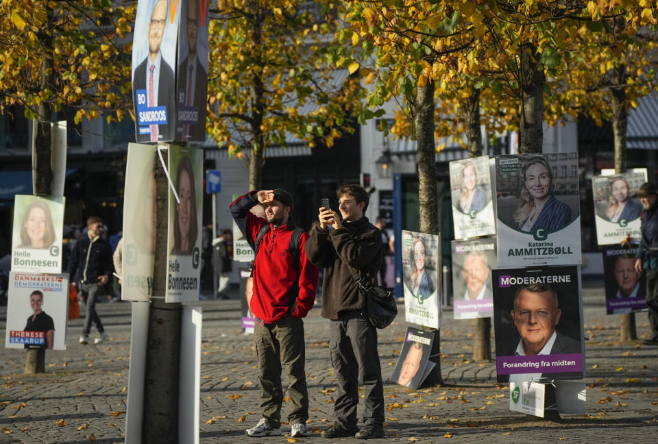 People stand near campaign posters in Copenhagen, Denmark, Sunday Oct. 30, 2022, ahead of the general election on November 1, 2022. (AP Photo/Sergei Grits)