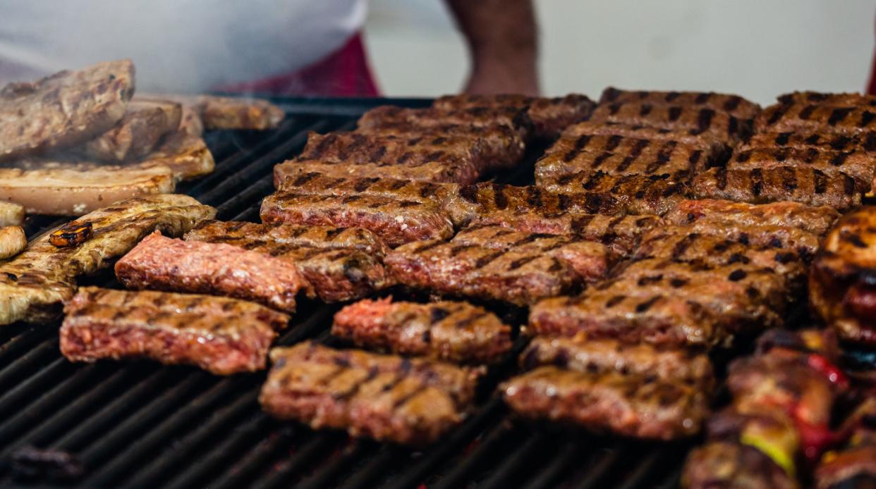 Juicy steaming meat on a charcoal grill, pork steaks, chicken breast, sausages, pieces of meat chops, Romanian minced meat (mici)  at a street food festival