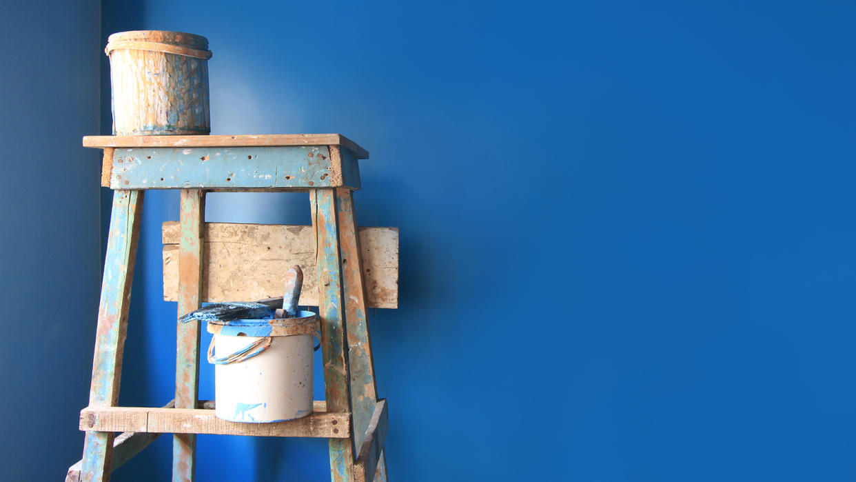 Paint cans on a dirty ladder in front of a wall freshly painted blue