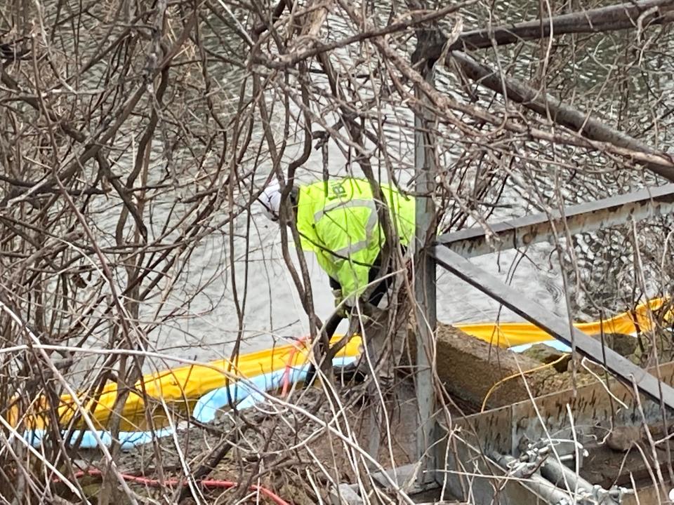 A member of the chemical spill mitigation team adjust booms (yellow) and absorbent snake-like booms (blue) along Otter Creek in Bristol after a chemical spill.