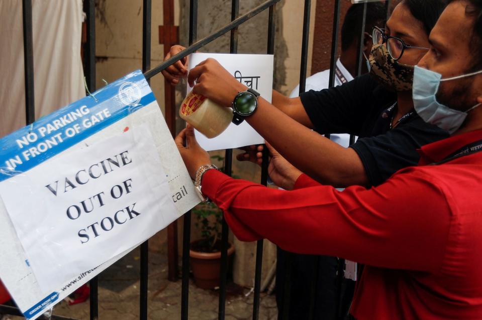 Two masked people in India hang a sign saying COVID-19 vaccines are out of stock