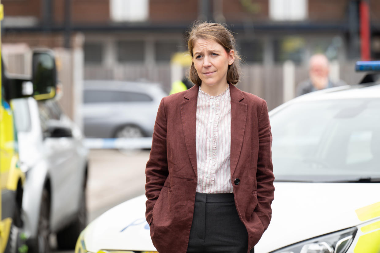  Sarah Collins standing with her hands in her pockets with police cars behind her. 