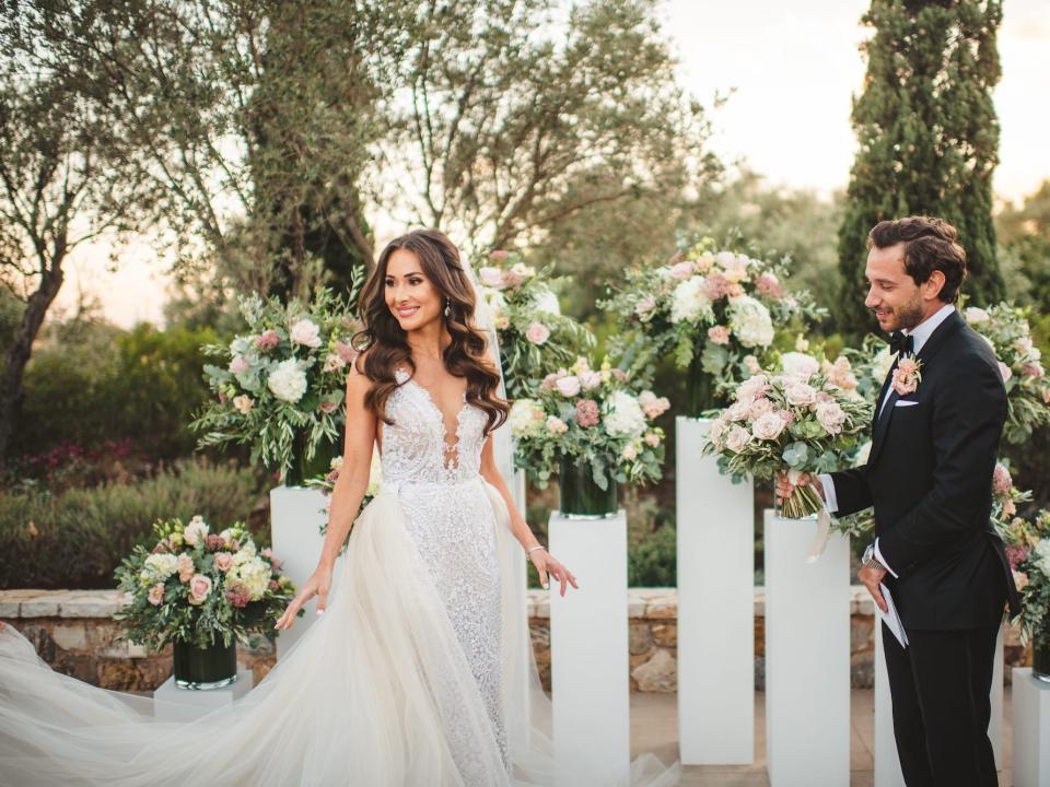 A bride looks over her shoulder as her groom holds her flowers at her wedding.