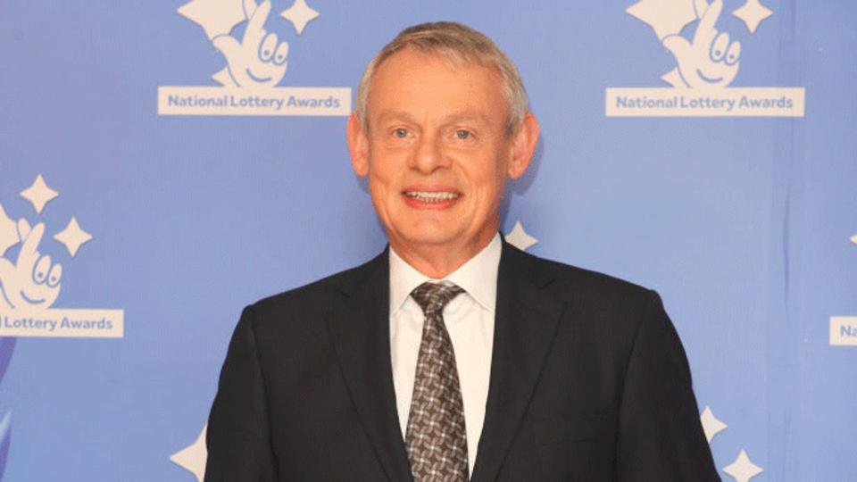 Martin Clunes wearing a black suit. 