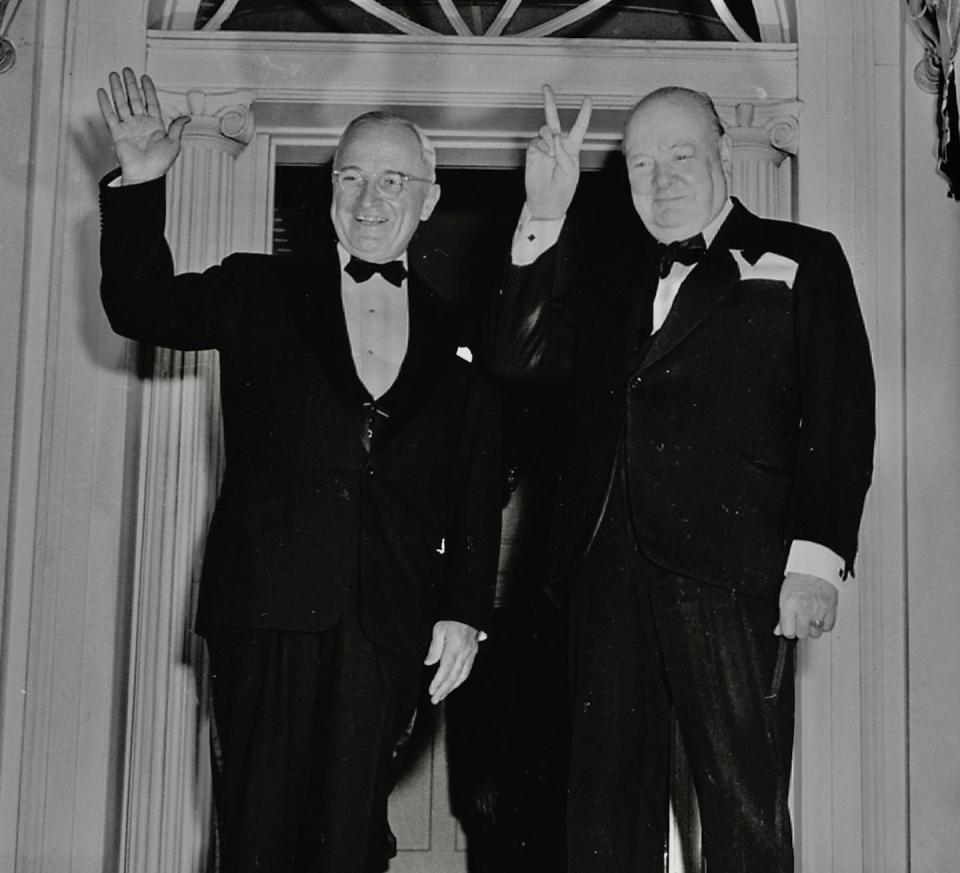 Winston Churchill hace la señal de victoria junto a Truman que hace un gesto de saludo con la mano en la puerta de la Blair House en Washington DC.