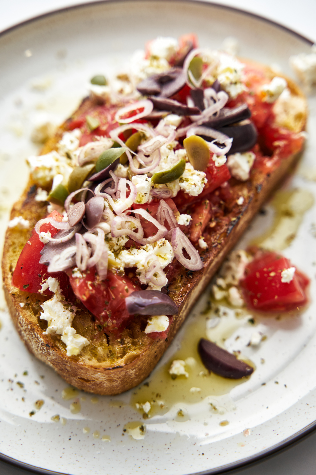 Closeup of Greek Bruschetta, traditional greek salad on a slice of bread, selective focus, on a brown-lined ceramic plate, blurred top background