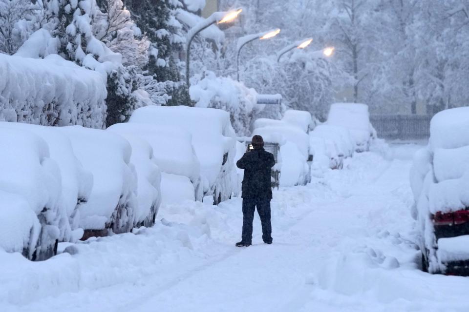 A man takes pictures of snow covered cars after heavy snow fall in Munich, Germany, Saturday, Dec. 2, 2023. (AP Photo/Matthias Schrader)