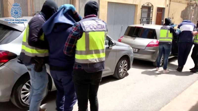 Men with heads covered with towels are led out of a building to the cars, in Almeria