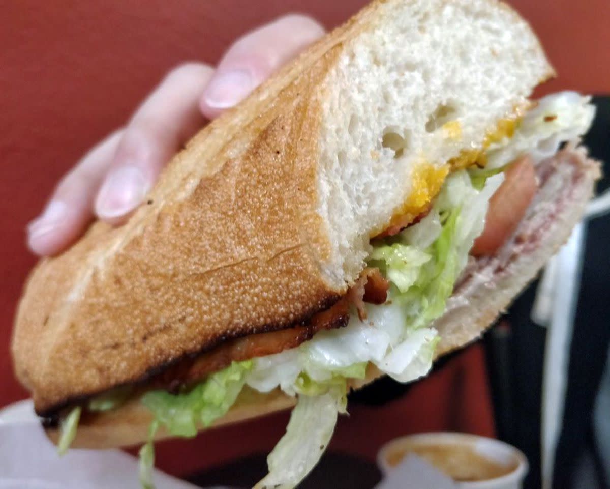 Right hand holding Joker's Dip Sandwich, Tub's Gourmet Subs, Seattle, red seating blurred in the background