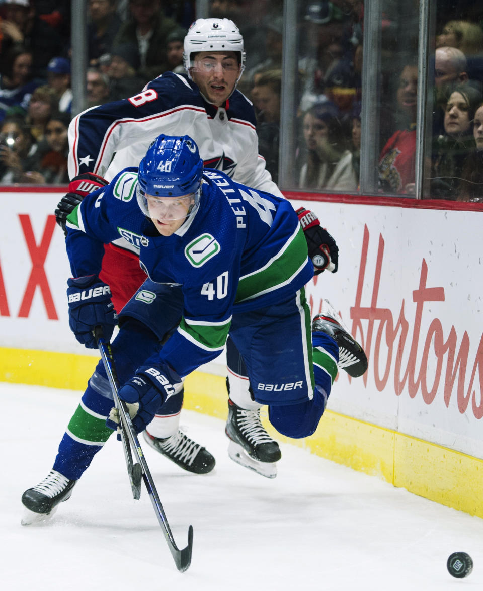 Vancouver Canucks center Elias Pettersson (40) fights for control of the puck with Columbus Blue Jackets defenseman Zach Werenski (8) during the second period of an NHL hockey game in Vancouver, British Columbia, Sunday, March 8, 2020. (Jonathan Hayward/The Canadian Press via AP)